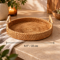 A round woven rattan tray with two light wood handles sits on a stone countertop in a warm, styled kitchen setting. A black dimension line across the bottom indicates the tray's width as 8.