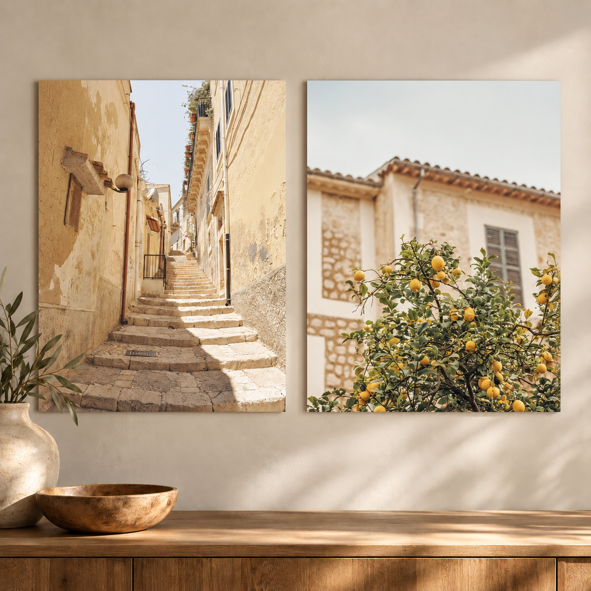 Two vertical wall art prints displayed side by side on a beige wall above a wooden console table. The left print shows a sunlit stone staircase between warm beige buildings.