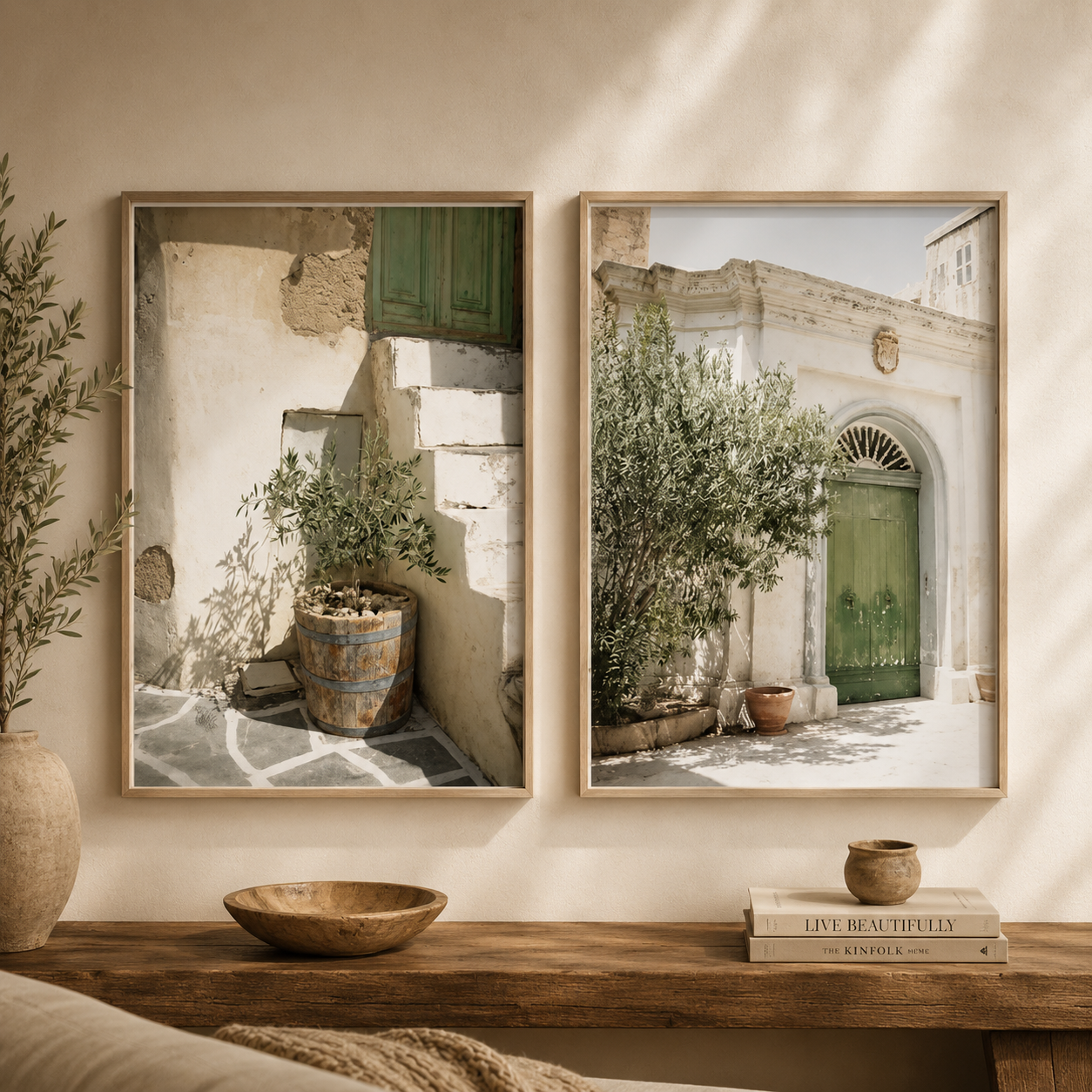 Two framed art prints depicting Mediterranean courtyard scenes with green doors and potted plants, displayed side-by-side on a beige wall above a wooden console table with decorative items.