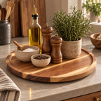 Round wooden serving tray styled on a kitchen counter with small bowls, a bottle of oil, wooden salt and pepper mills, and a potted rosemary plant.
