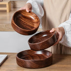 Person holding a set of wooden bowls on a wooden table.