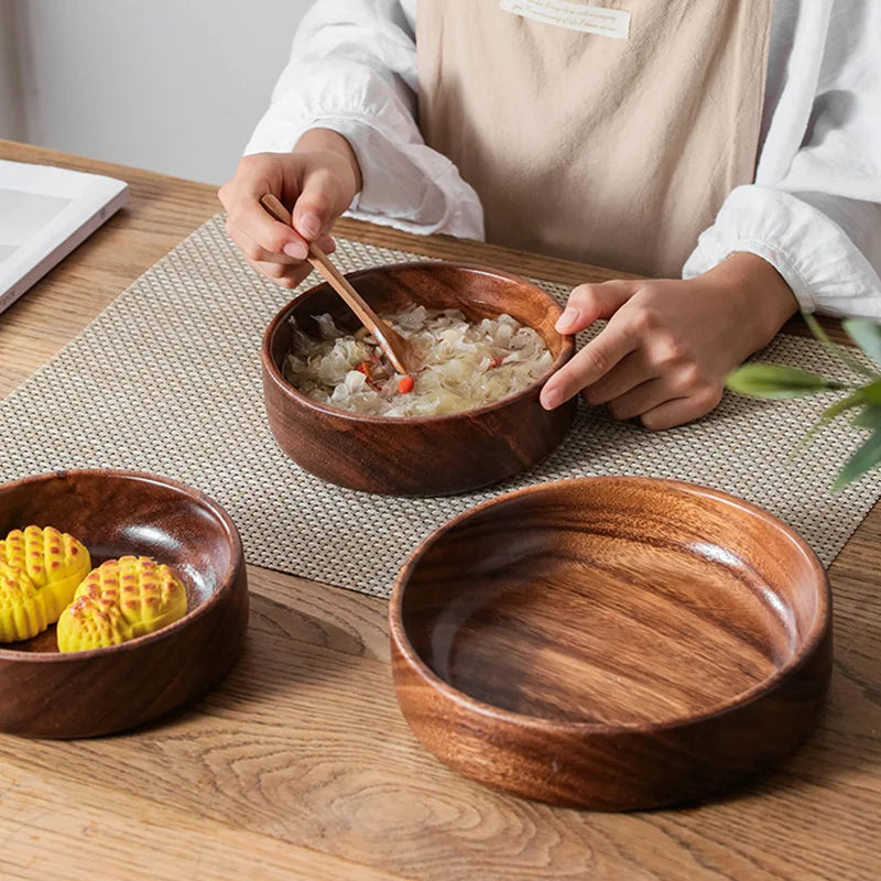 Person eating from a wooden bowl on a wooden table with other wooden bowls and food items.