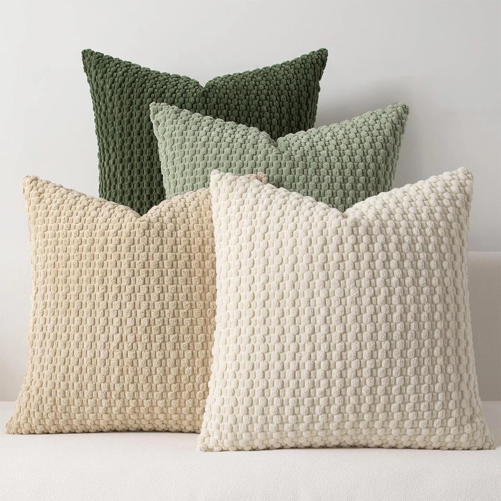 Four textured pillows in green, beige, and white on a light background
