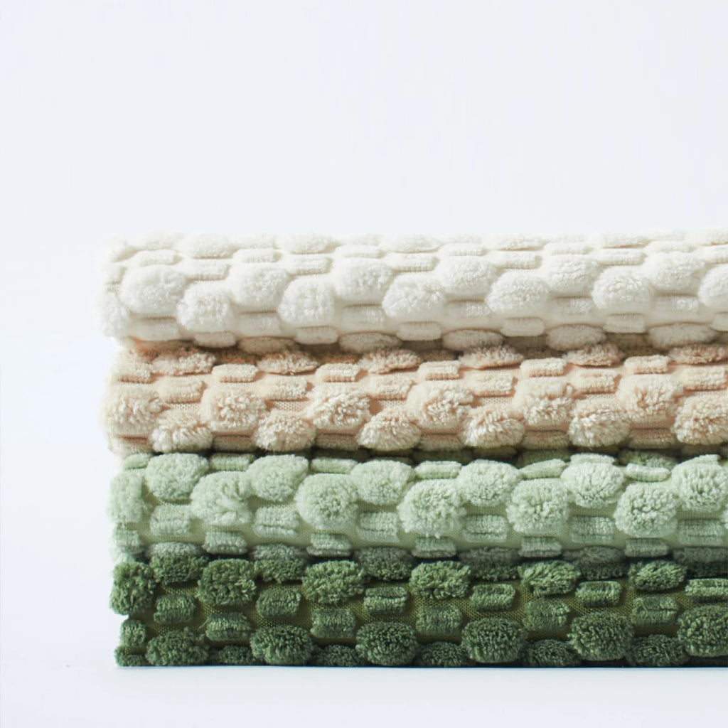 Stack of textured pillow covers in beige, pink, and green on a white background