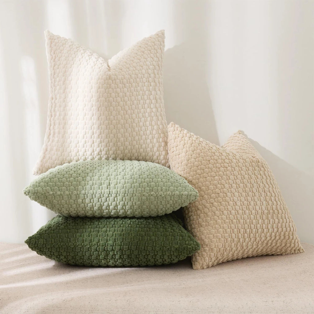 Stack of textured pillows in beige, green, and light green on a neutral background