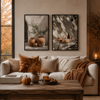Two framed art prints with warm autumnal tones hang on a beige wall above a cream sofa styled with brown and beige pillows, a rust throw blanket, and a wooden coffee table in a cozy living room.