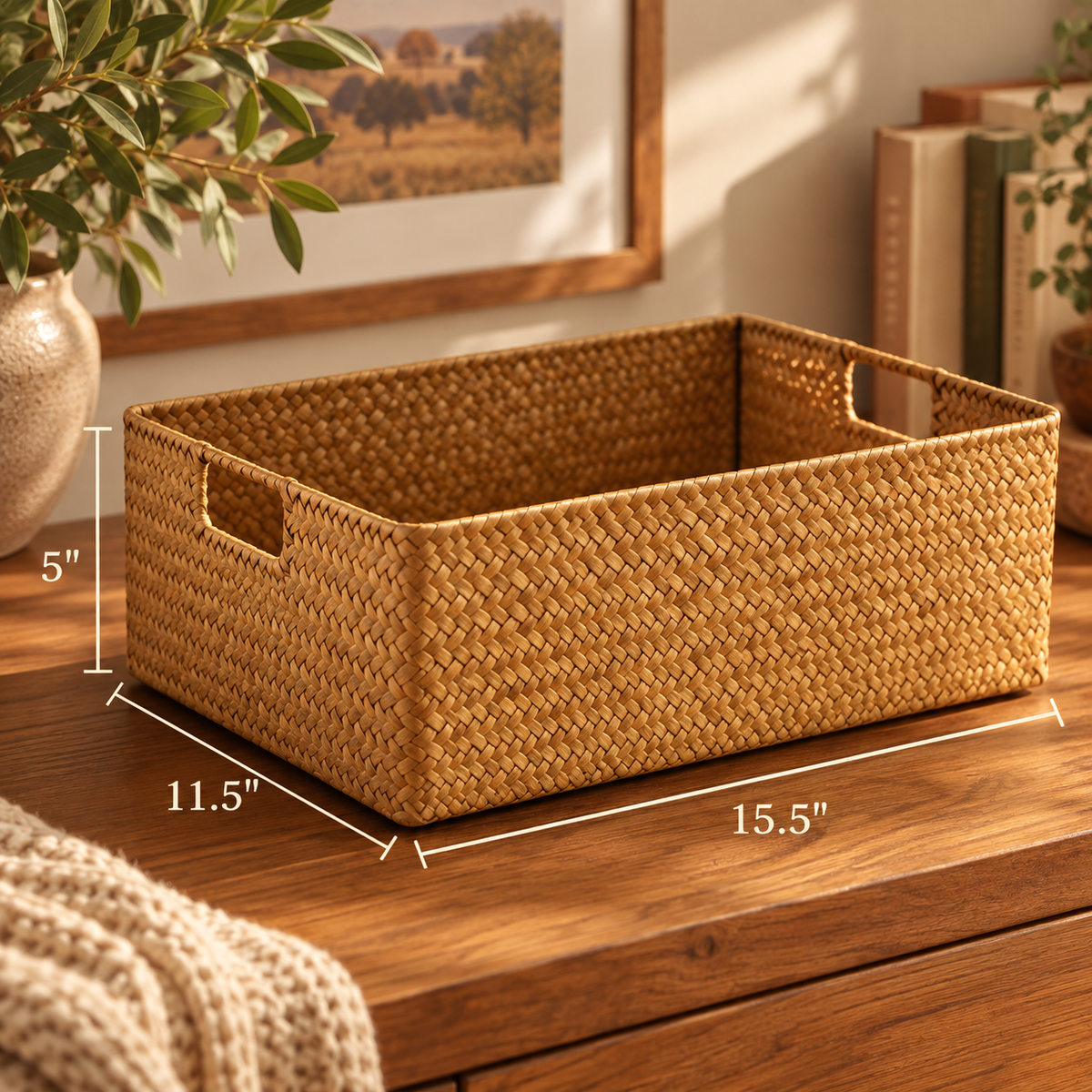 A woven rectangular storage basket with cutout side handles sits on a wooden table in a styled room. White dimension lines and text show the basket's measurements: 15.
