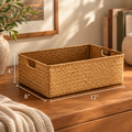 A woven rectangular storage basket with cutout handles sits on a wooden table in a styled room setting. White dimension lines and text show the basket's measurements: 12 inches wide, 8 inches deep, and 4 inches tall.