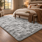 A large, plush shag area rug in a light gray and white mottled pattern, styled in a modern, warm-toned bedroom next to a wooden bed and bench.