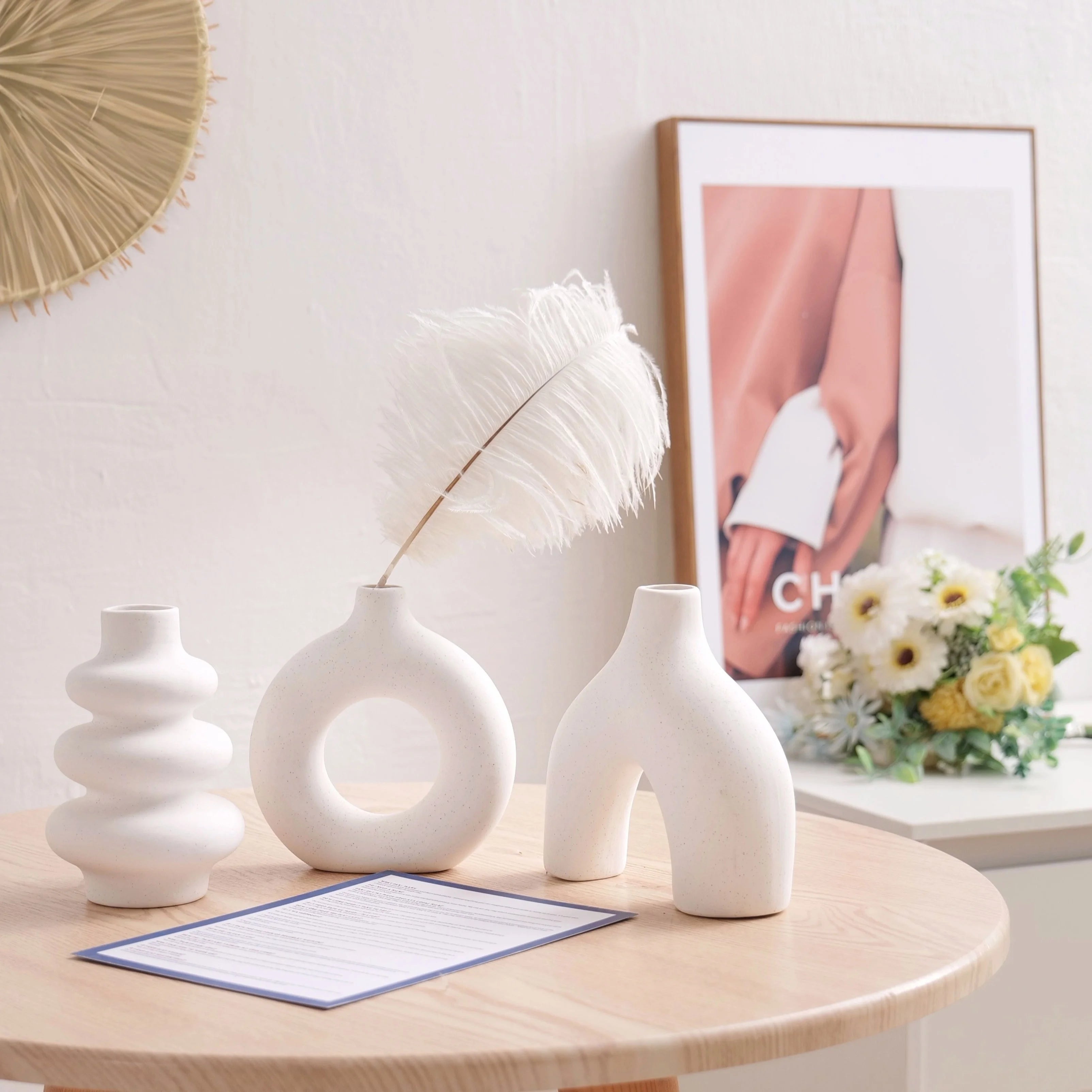 Three white ceramic vases on a wooden table with a decorative frame and flowers in the background.